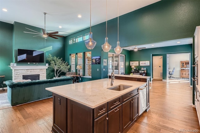 kitchen with light stone counters, pendant lighting, open floor plan, dark brown cabinetry, and a sink