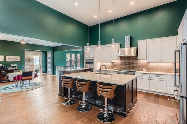 kitchen with white cabinets, decorative light fixtures, and wall chimney range hood