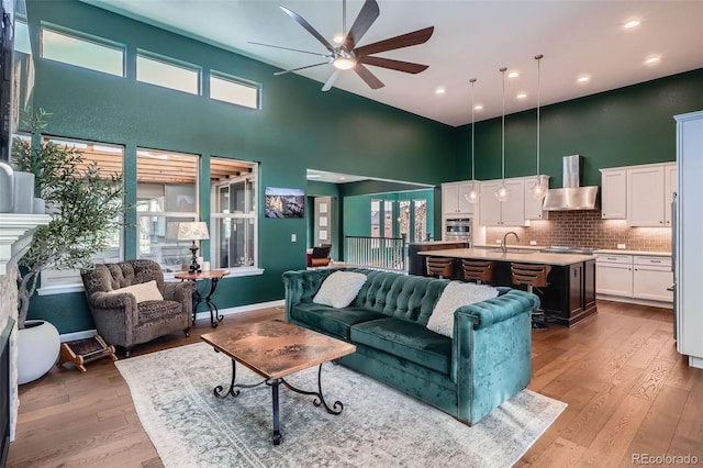 living area featuring a towering ceiling, light wood finished floors, a ceiling fan, and recessed lighting