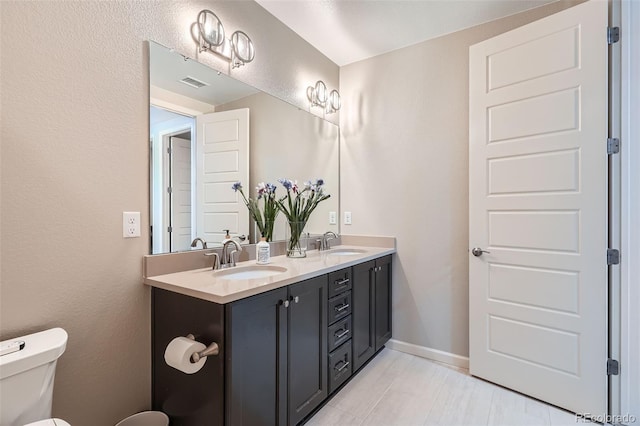 bathroom featuring toilet, double vanity, a sink, and visible vents