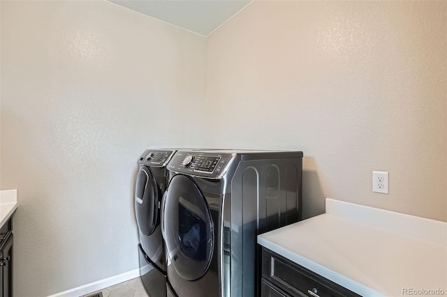 clothes washing area with light tile patterned floors, washer and clothes dryer, cabinet space, and baseboards