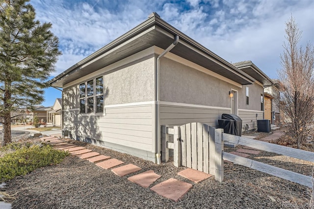 view of property exterior with central air condition unit, a garage, fence, and stucco siding