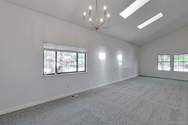 carpeted empty room with vaulted ceiling with skylight and a chandelier