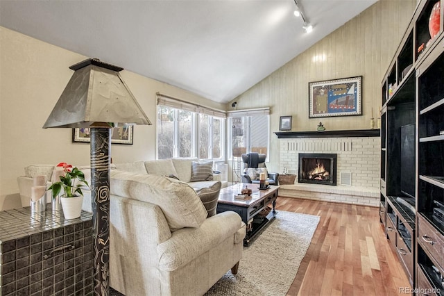 living room featuring rail lighting, vaulted ceiling, a brick fireplace, and light hardwood / wood-style flooring