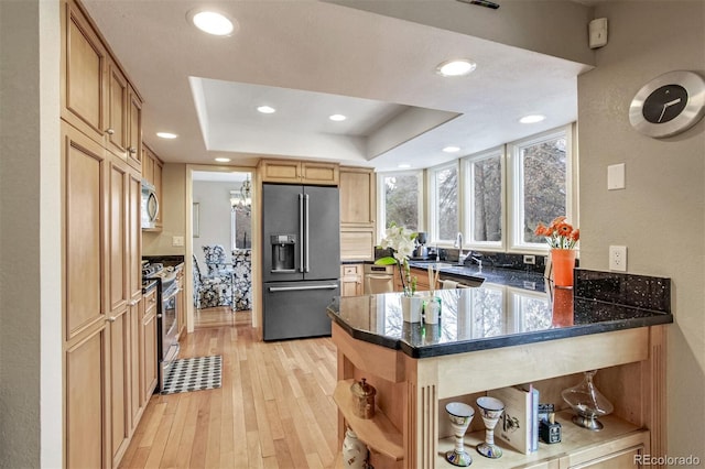 kitchen with high end black fridge, a tray ceiling, light hardwood / wood-style floors, stainless steel range oven, and kitchen peninsula