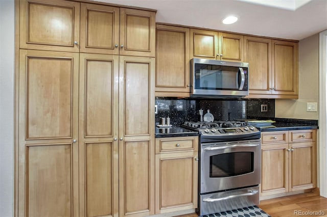 kitchen with stainless steel appliances, tasteful backsplash, light wood-type flooring, and dark stone counters