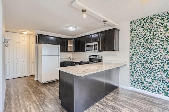 kitchen with kitchen peninsula, a textured ceiling, appliances with stainless steel finishes, and light wood-type flooring