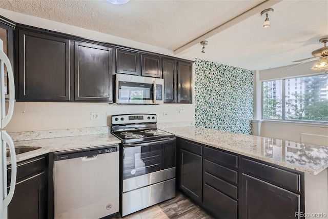 kitchen featuring ceiling fan, stainless steel appliances, light stone counters, and a textured ceiling