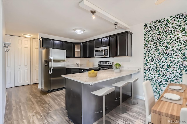 kitchen featuring light stone counters, kitchen peninsula, light wood-type flooring, a breakfast bar area, and appliances with stainless steel finishes