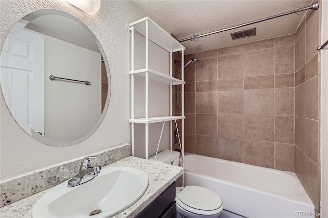 full bathroom with toilet, a textured ceiling, tiled shower / bath, and vanity