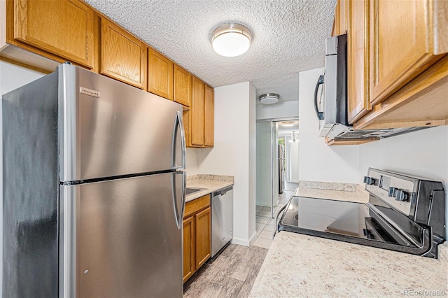2225 Buchtel Blvd Unit 208, Denver, CO 80210 - kitchen with appliances with stainless steel finishes, light countertops, brown cabinets, a textured ceiling, and light wood-style floors