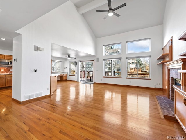 unfurnished living room featuring visible vents, baseboards, a tiled fireplace, beamed ceiling, and light wood-style floors