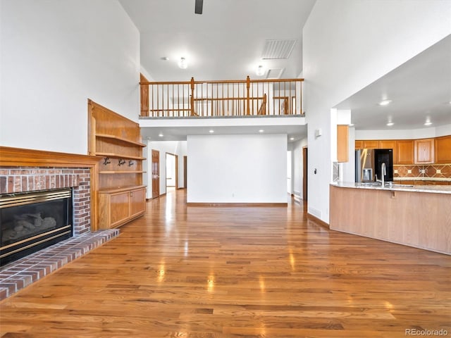 living area with wood finished floors, visible vents, baseboards, a towering ceiling, and a brick fireplace