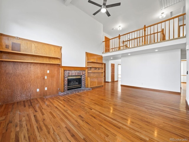 unfurnished living room with a brick fireplace, wood finished floors, a high ceiling, and ceiling fan