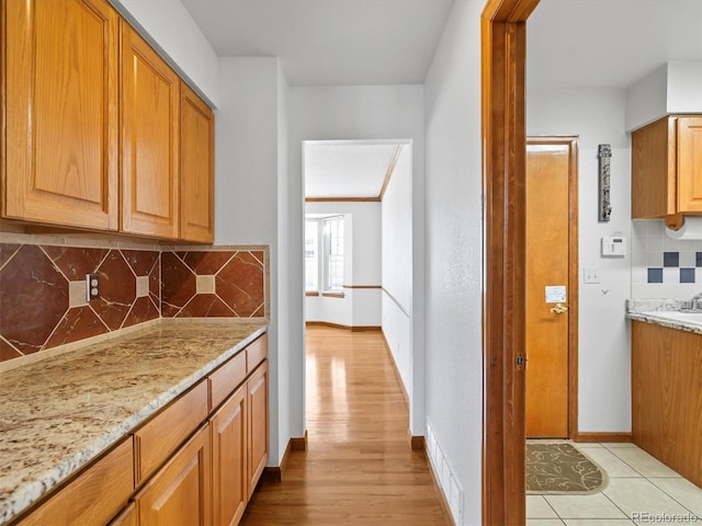 kitchen featuring light stone countertops, tasteful backsplash, light wood finished floors, and baseboards