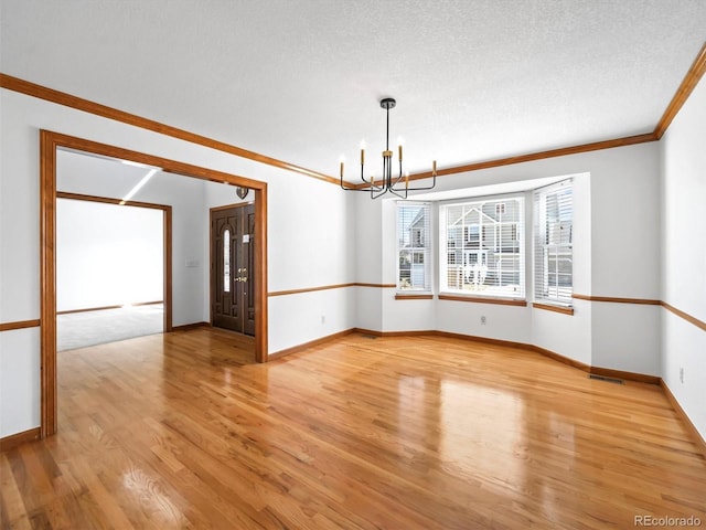 spare room with light wood finished floors, crown molding, baseboards, a notable chandelier, and a textured ceiling