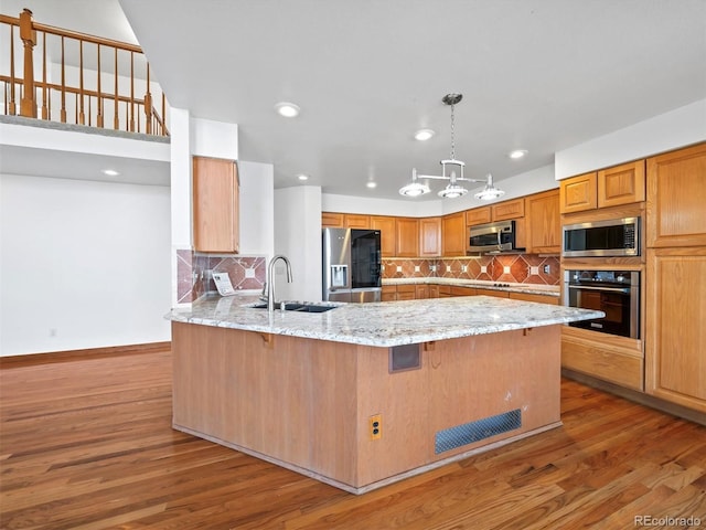 kitchen with wood finished floors, light stone countertops, a peninsula, a sink, and stainless steel appliances