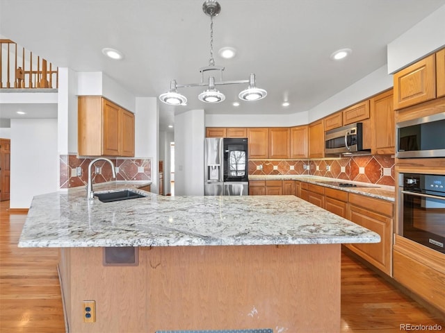 kitchen with a sink, light stone counters, stainless steel appliances, light wood-style floors, and a peninsula