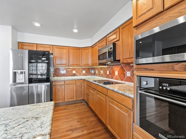 kitchen with black appliances, light stone counters, light wood-style floors, and backsplash