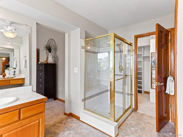 bathroom featuring vanity, a shower stall, a walk in closet, and baseboards