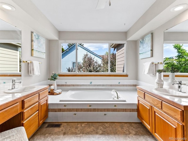 bathroom featuring two vanities, a garden tub, and a sink