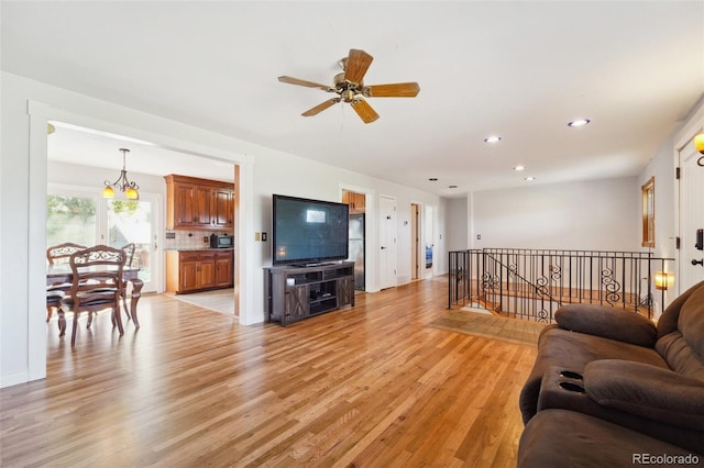 living room with ceiling fan with notable chandelier and light hardwood / wood-style floors