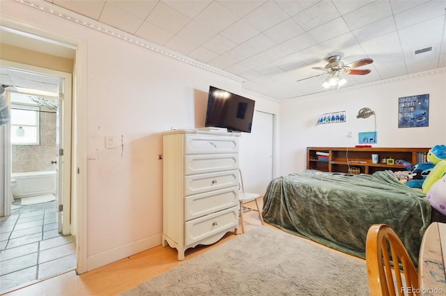 bedroom featuring light wood-type flooring, ornamental molding, ensuite bath, and ceiling fan