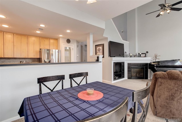 dining space with a tiled fireplace, light colored carpet, and ceiling fan