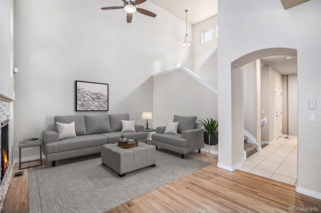 living room with stairway, high vaulted ceiling, light wood-type flooring, arched walkways, and a ceiling fan