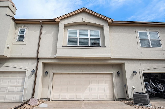 exterior space with concrete driveway, an attached garage, central AC unit, and stucco siding