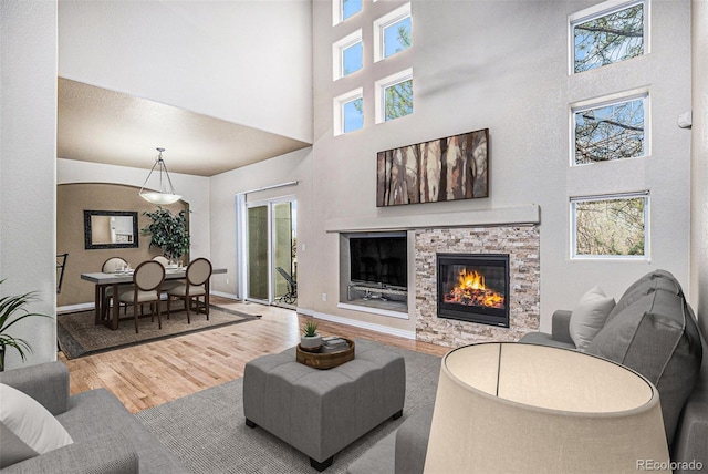 living area with a fireplace, baseboards, wood finished floors, and a towering ceiling