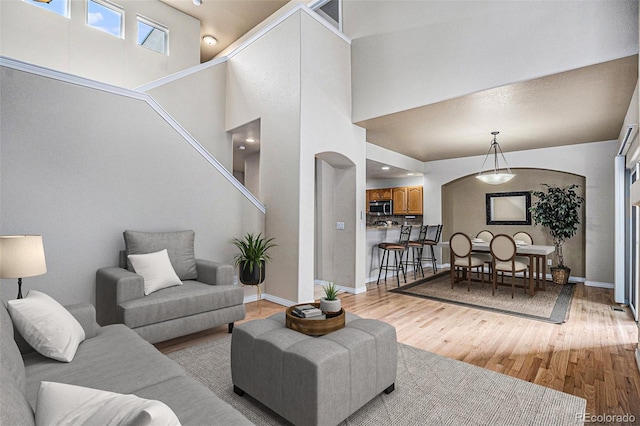 living area featuring arched walkways, baseboards, a high ceiling, and light wood-type flooring
