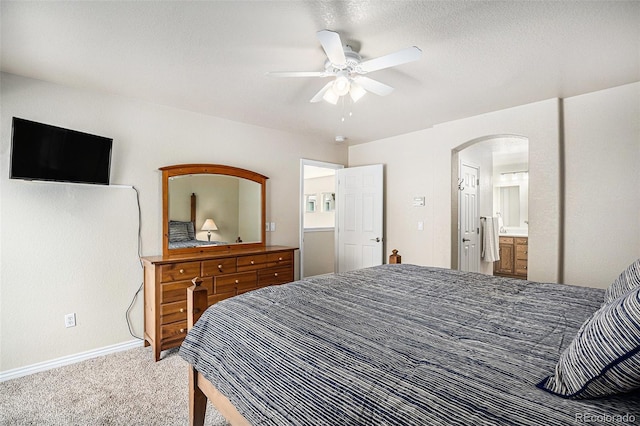 carpeted bedroom with baseboards, arched walkways, a ceiling fan, and ensuite bath