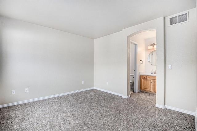unfurnished bedroom with visible vents, arched walkways, carpet, and baseboards