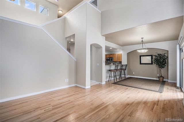 living area featuring arched walkways, baseboards, a high ceiling, and light wood finished floors