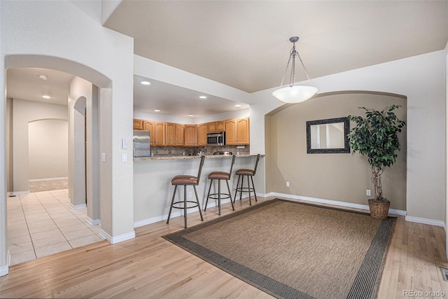 kitchen featuring a kitchen bar, appliances with stainless steel finishes, tasteful backsplash, arched walkways, and light wood-type flooring