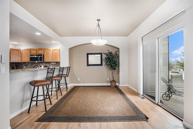 kitchen featuring light wood-style floors, a breakfast bar area, stainless steel microwave, baseboards, and decorative backsplash