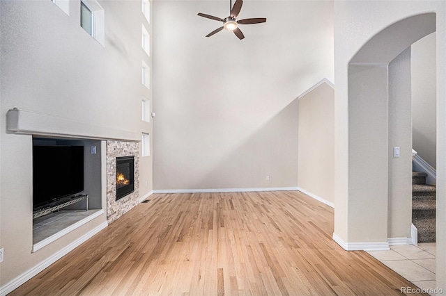 unfurnished living room with ceiling fan, a stone fireplace, wood finished floors, stairway, and baseboards