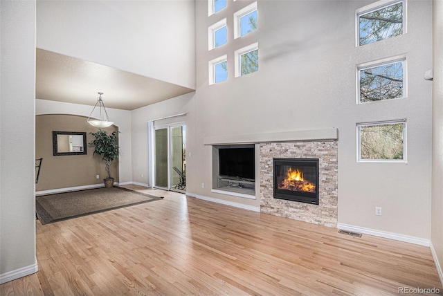 unfurnished living room with a healthy amount of sunlight, a high ceiling, a fireplace, and wood finished floors