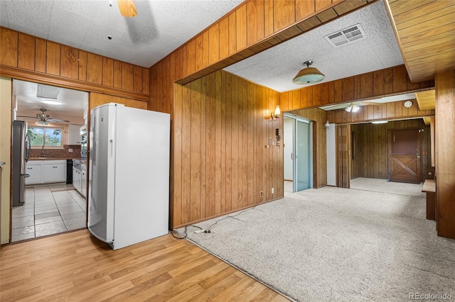 1280 Xanadu St, Aurora, CO 80011 - kitchen featuring freestanding refrigerator, ceiling fan, wooden walls, light wood finished floors, and brown cabinetry