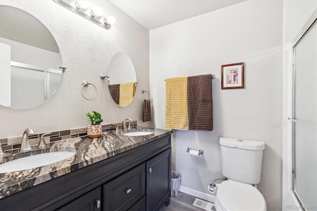 bathroom featuring toilet, visible vents, a shower with door, and a sink