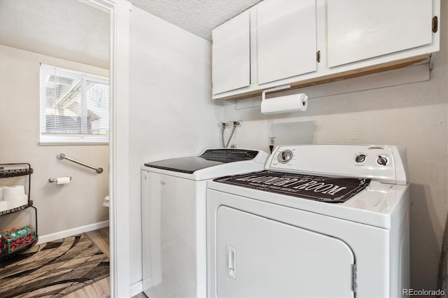 clothes washing area with wood finished floors, cabinet space, washer and clothes dryer, a textured ceiling, and baseboards