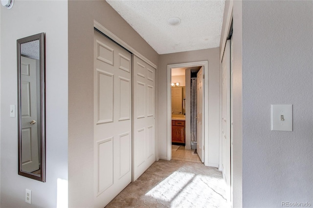 corridor with light carpet and a textured ceiling