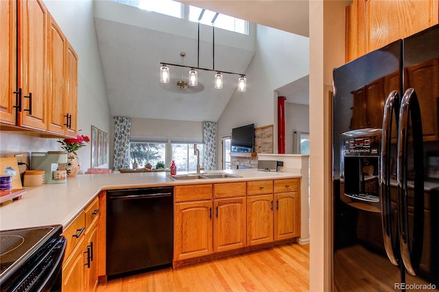 kitchen with sink, vaulted ceiling, kitchen peninsula, light hardwood / wood-style floors, and black appliances