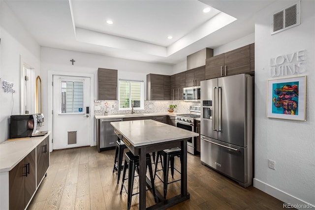 2824 W Parkside Pl, Denver, CO 80221 - kitchen featuring stainless steel appliances, a tray ceiling, dark brown cabinets, visible vents, and backsplash