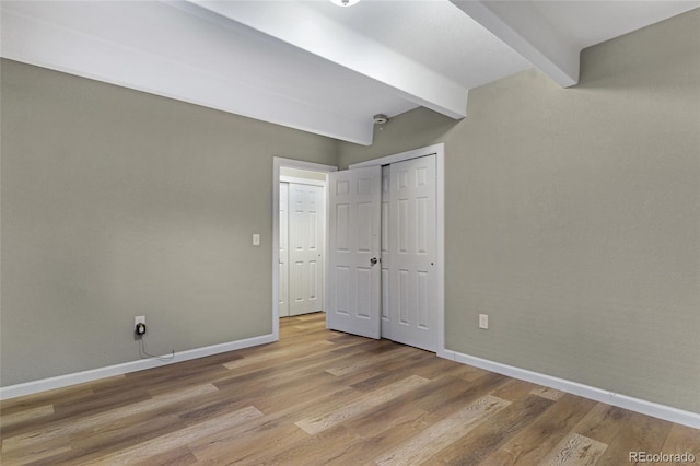 unfurnished bedroom featuring a closet, hardwood / wood-style floors, and beamed ceiling