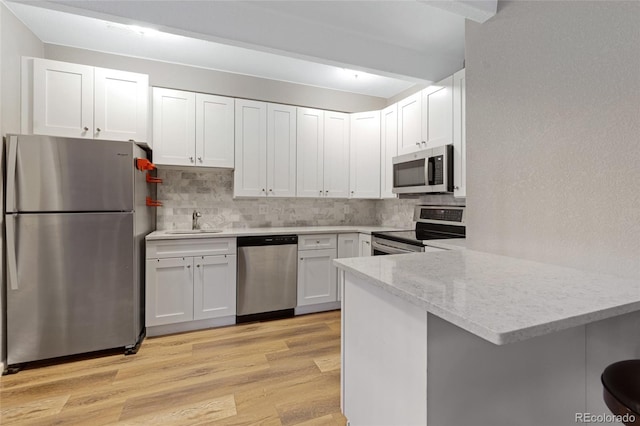 kitchen featuring kitchen peninsula, sink, light wood-type flooring, appliances with stainless steel finishes, and white cabinets