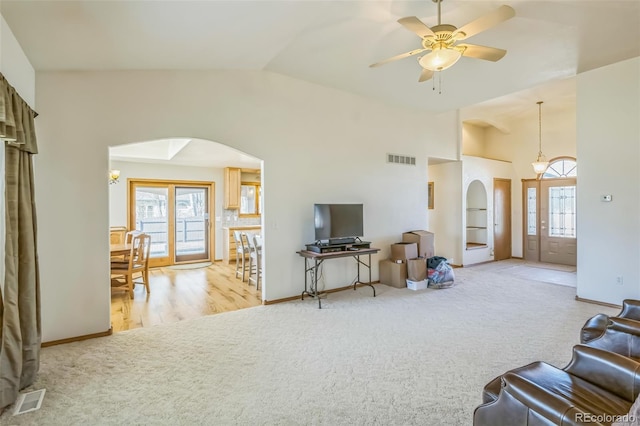 living area with a ceiling fan, arched walkways, carpet, and visible vents