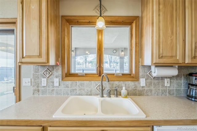 kitchen featuring light countertops, decorative backsplash, dishwasher, a sink, and light brown cabinetry