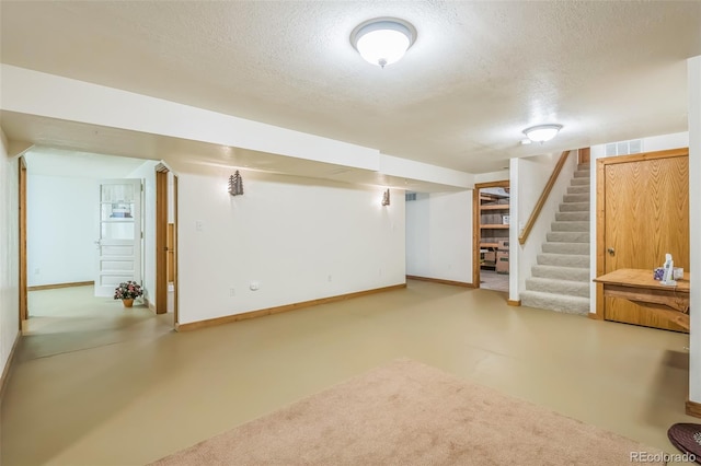 finished below grade area with a textured ceiling, baseboards, and stairs